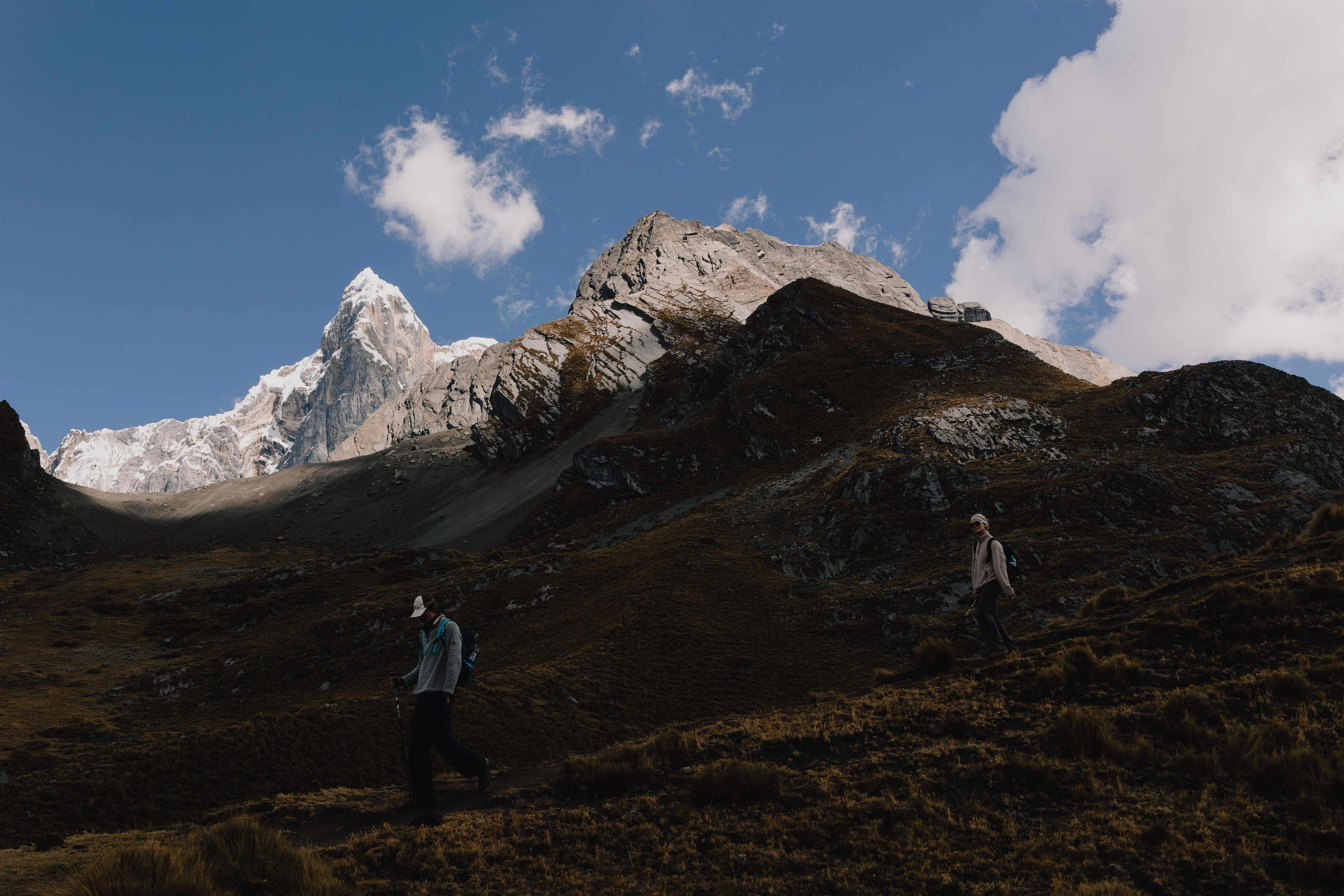 Huayhuash – Wanderer steigt einen Grat hoch, dahinter ein spitzer schneebedeckter Gipfel
