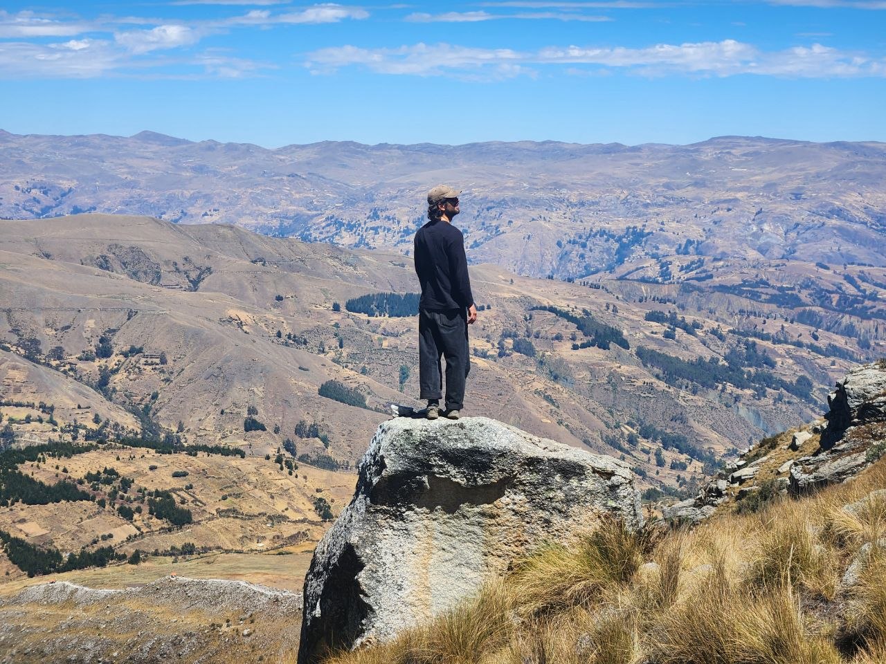 Huayhuash – Wanderer auf einem Felsblock mit Blick über das weite Tal bei Huaraz